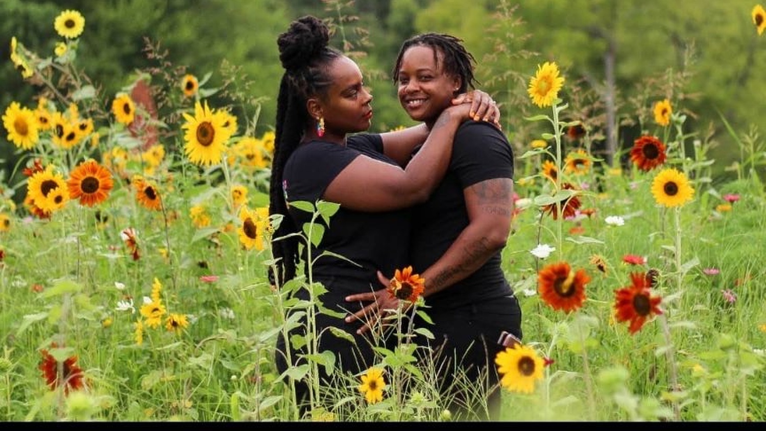 A couple stand in a field of sunflowers posing. 