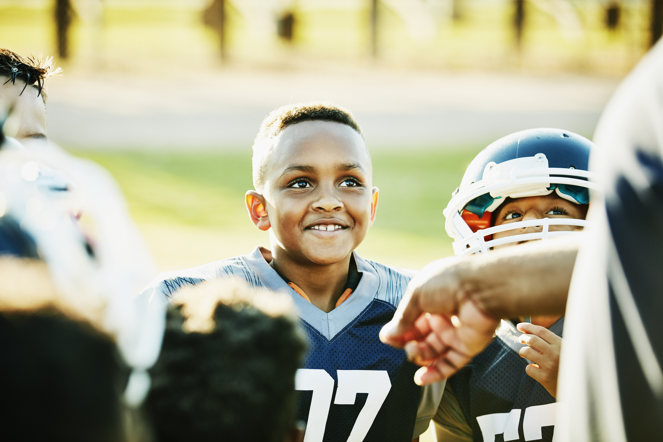 Smiling young football player listening to coach with teammates after game