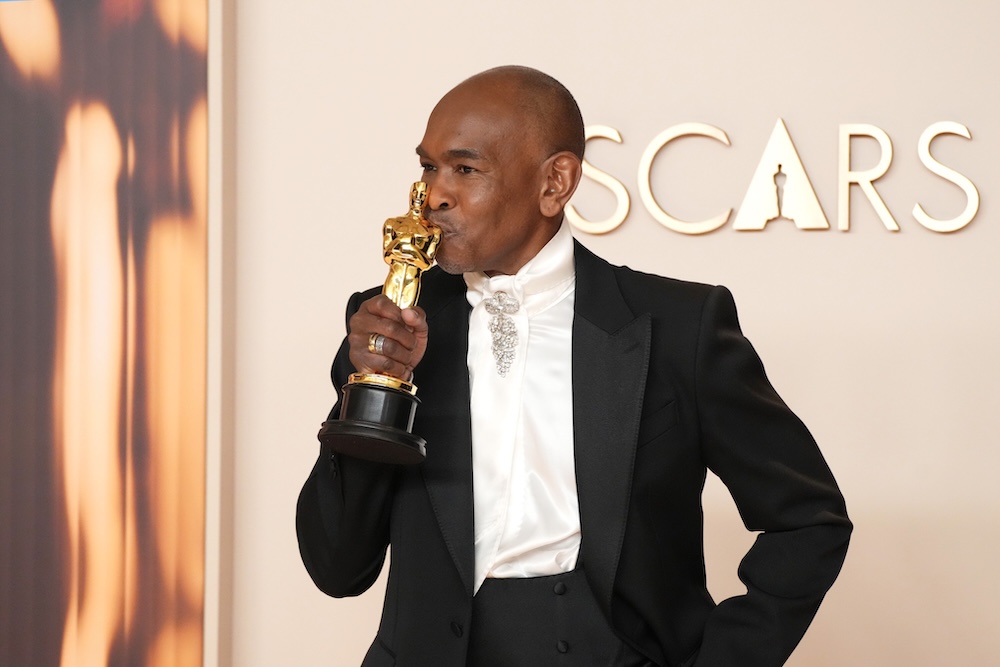 Person in tuxedo kisses an Oscar statue at an awards ceremony.
