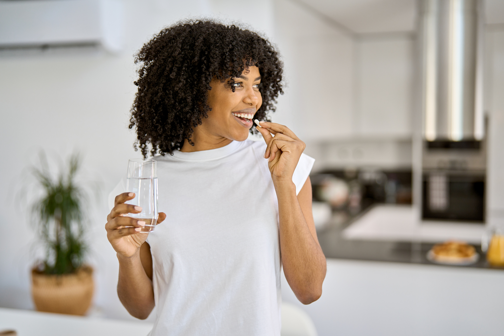 Happy healthy young African woman talking pill in the kitchen at home.
